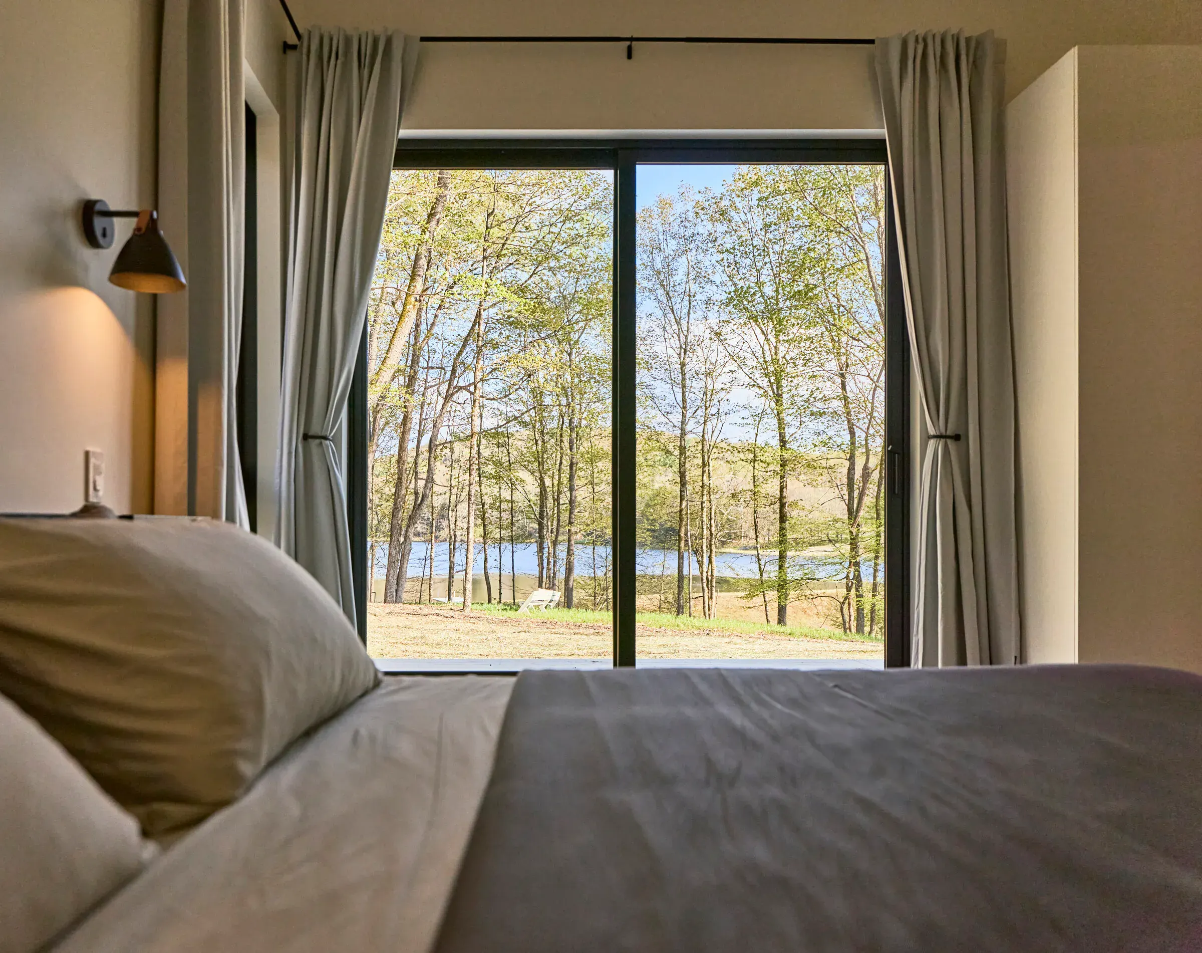 Bedroom at Verdant Sound — linen bed with a floor-to-ceiling window framing the private lake
