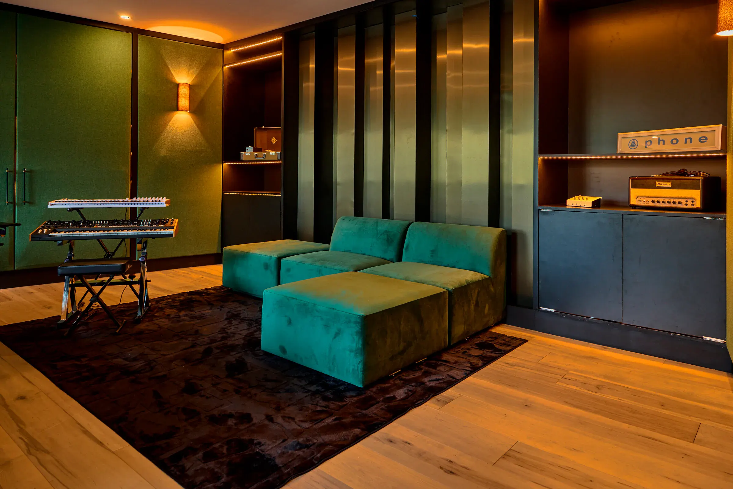 Verdant Sound control room lounge — green velvet sectional, synth rack, warm cove lighting
