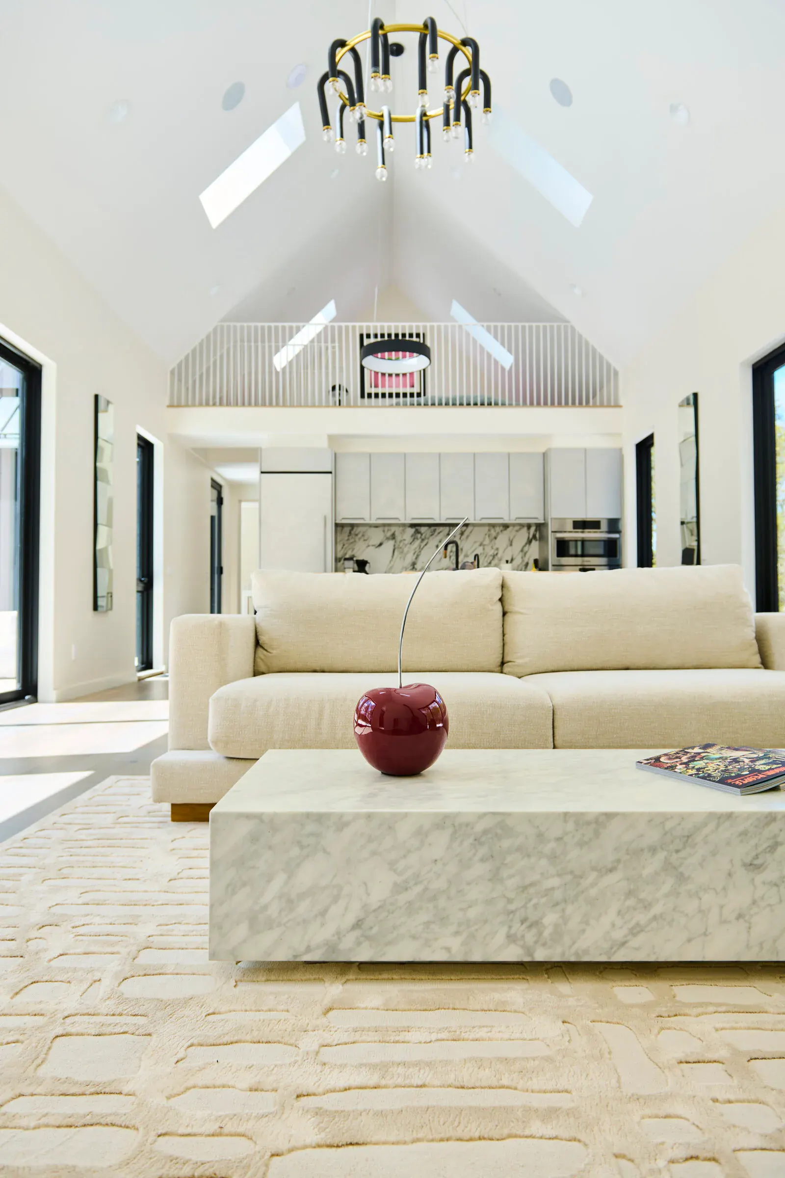 Open-plan kitchen and living space at Verdant Sound — marble coffee table, cream sofa, loft above
