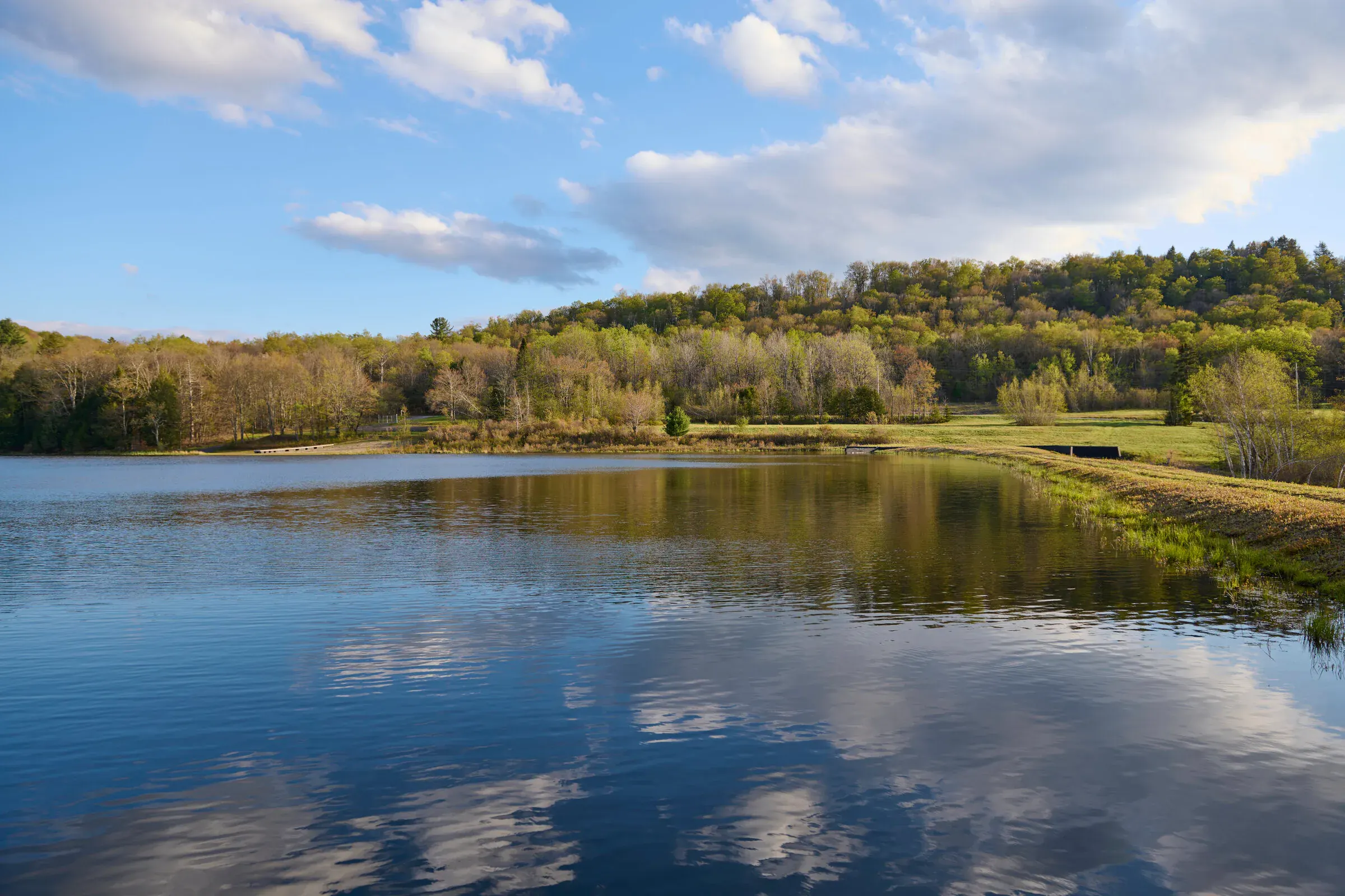 Private lake at Verdant Sound — wide view with clouds reflected on the water and rolling Catskills hills