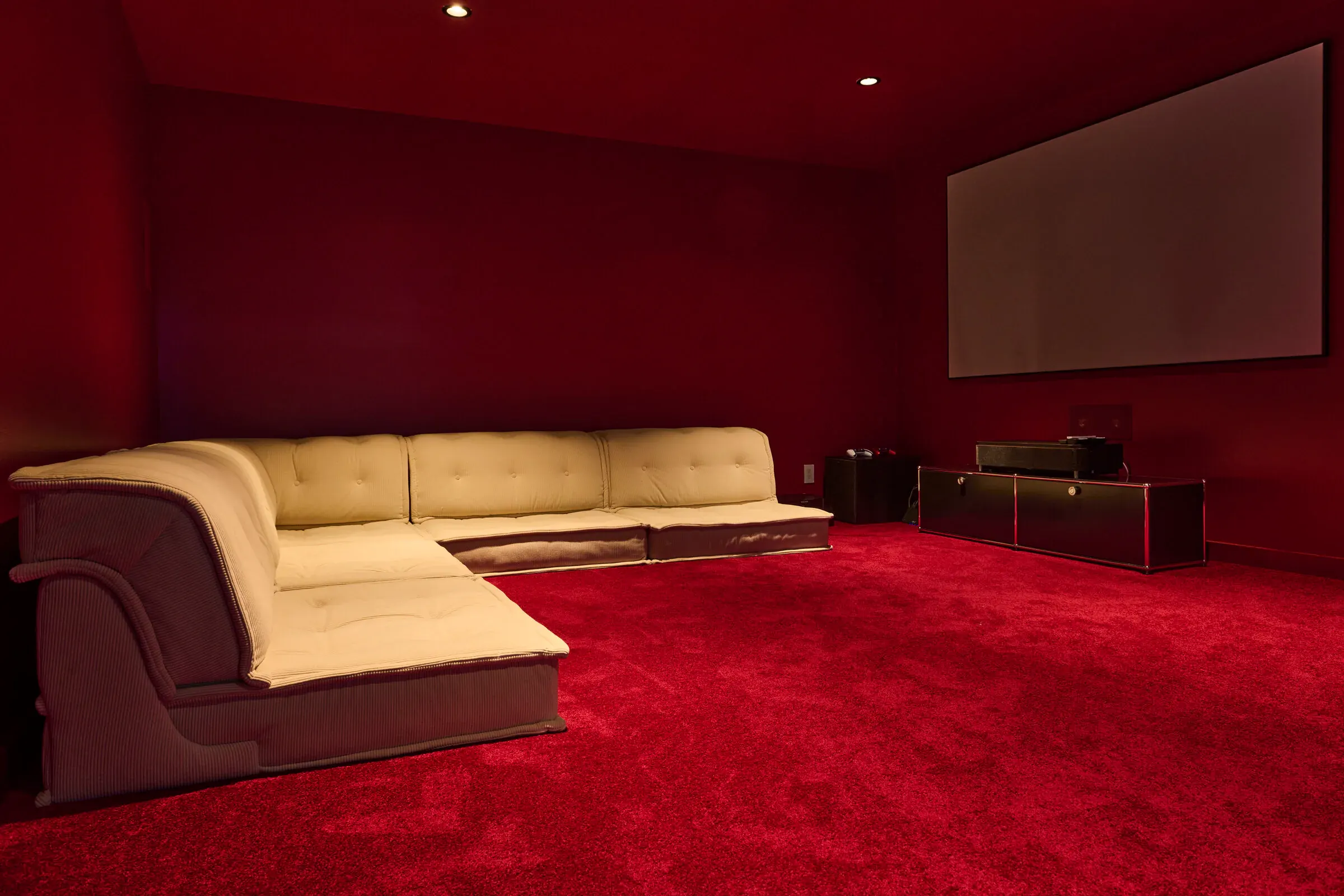 Verdant Sound subterranean theater — deep red carpet, cream sectional, and a large projection screen